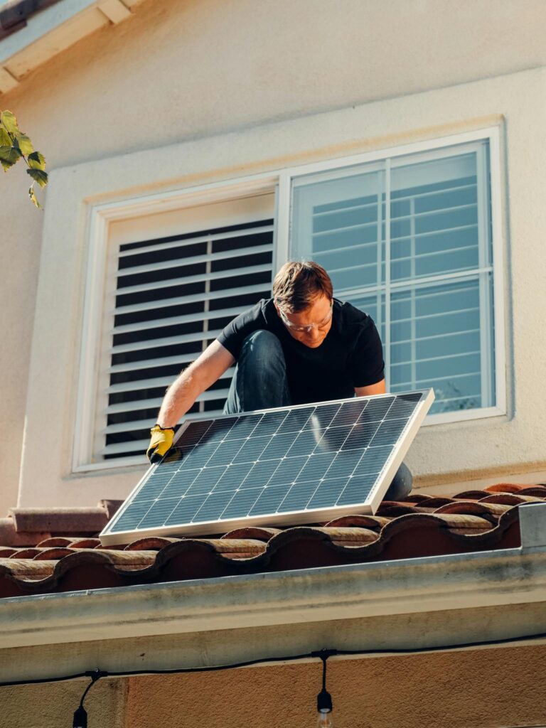 A worker installing a solar panel on a residential rooftop under bright sunlight.