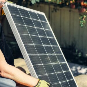 A worker installs a solar panel in a garden, promoting clean energy.