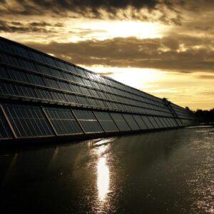 Silhouetted solar panels reflect sunset in tranquil waters, showcasing renewable energy.